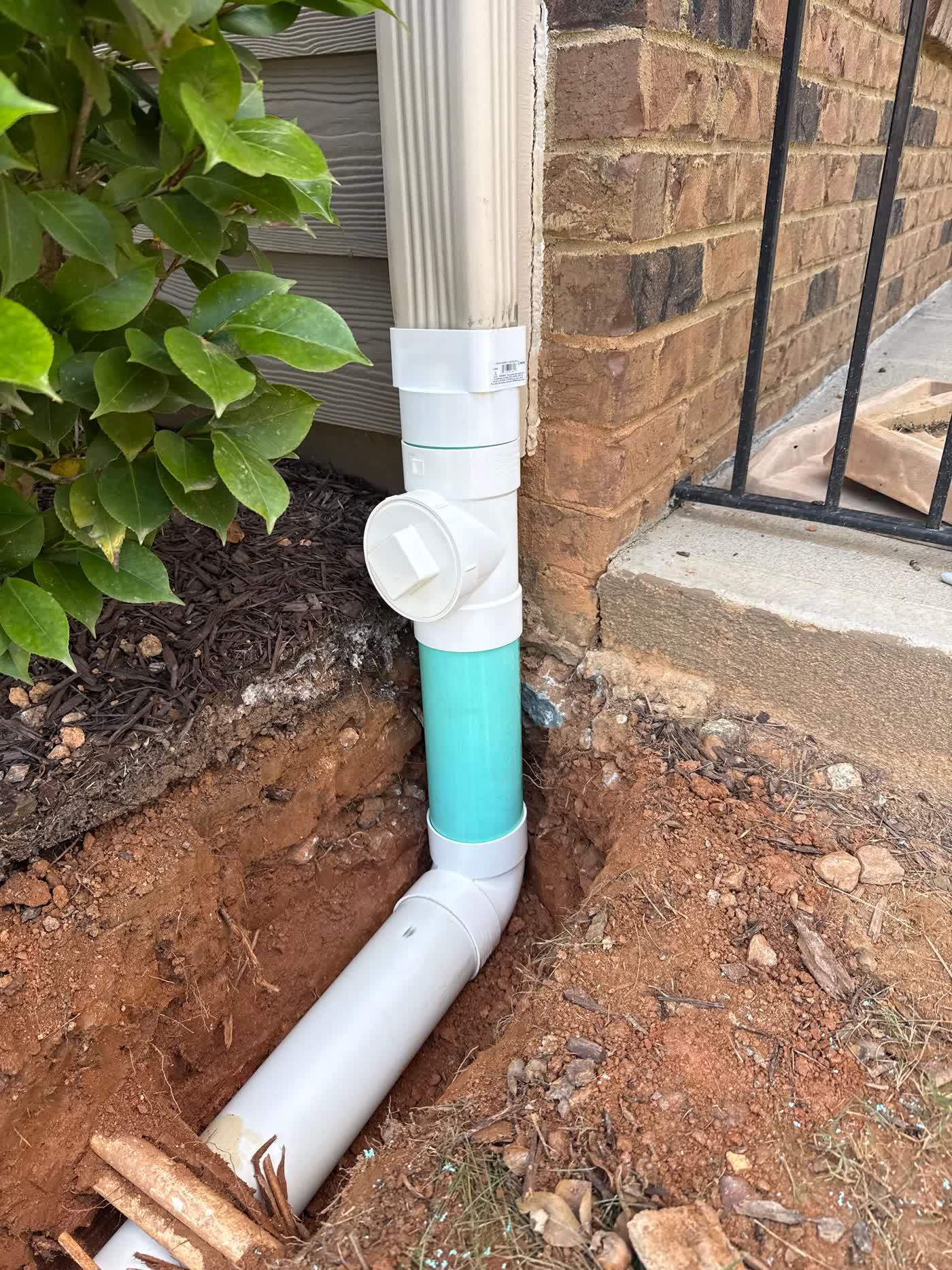Downspout tied into buried drain pipe beside a foundation