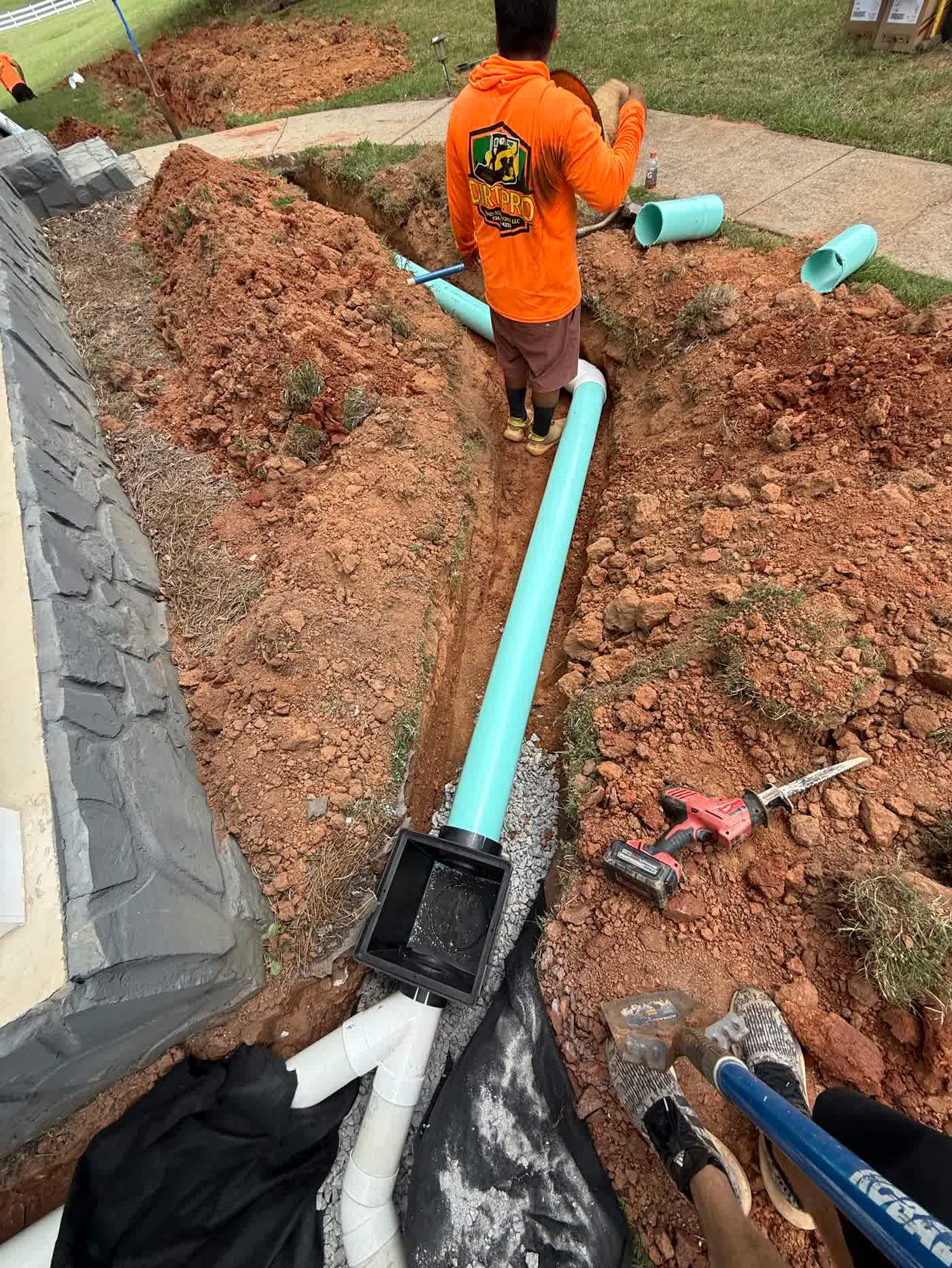 Crew running drain pipe through a trench beside a home
