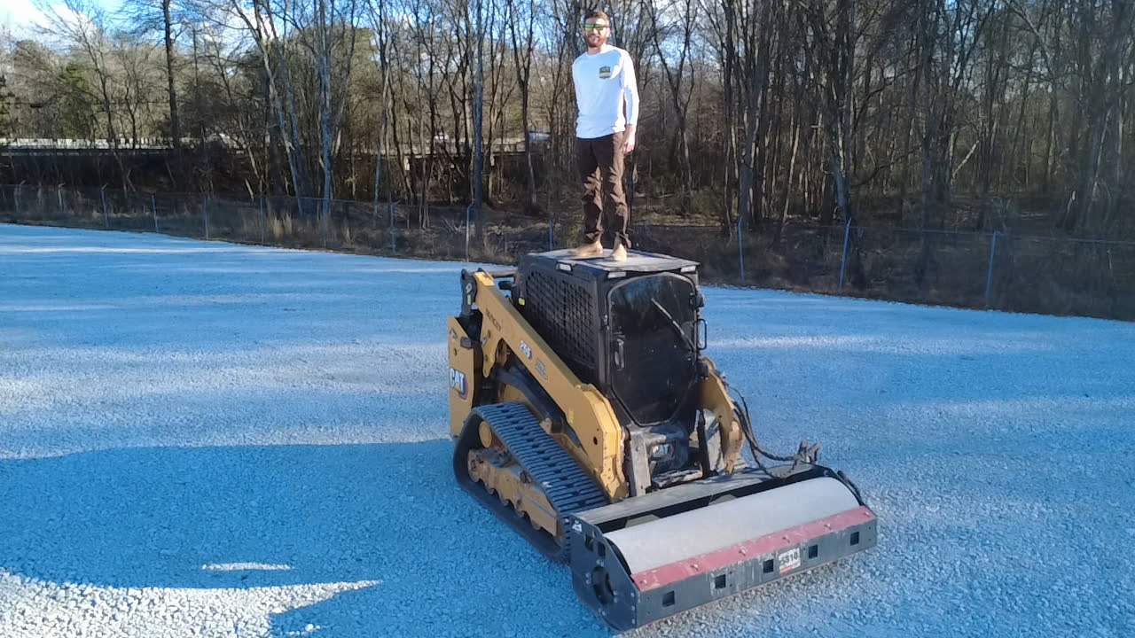 Skid steer with a roller compacting the base of a blue sport court