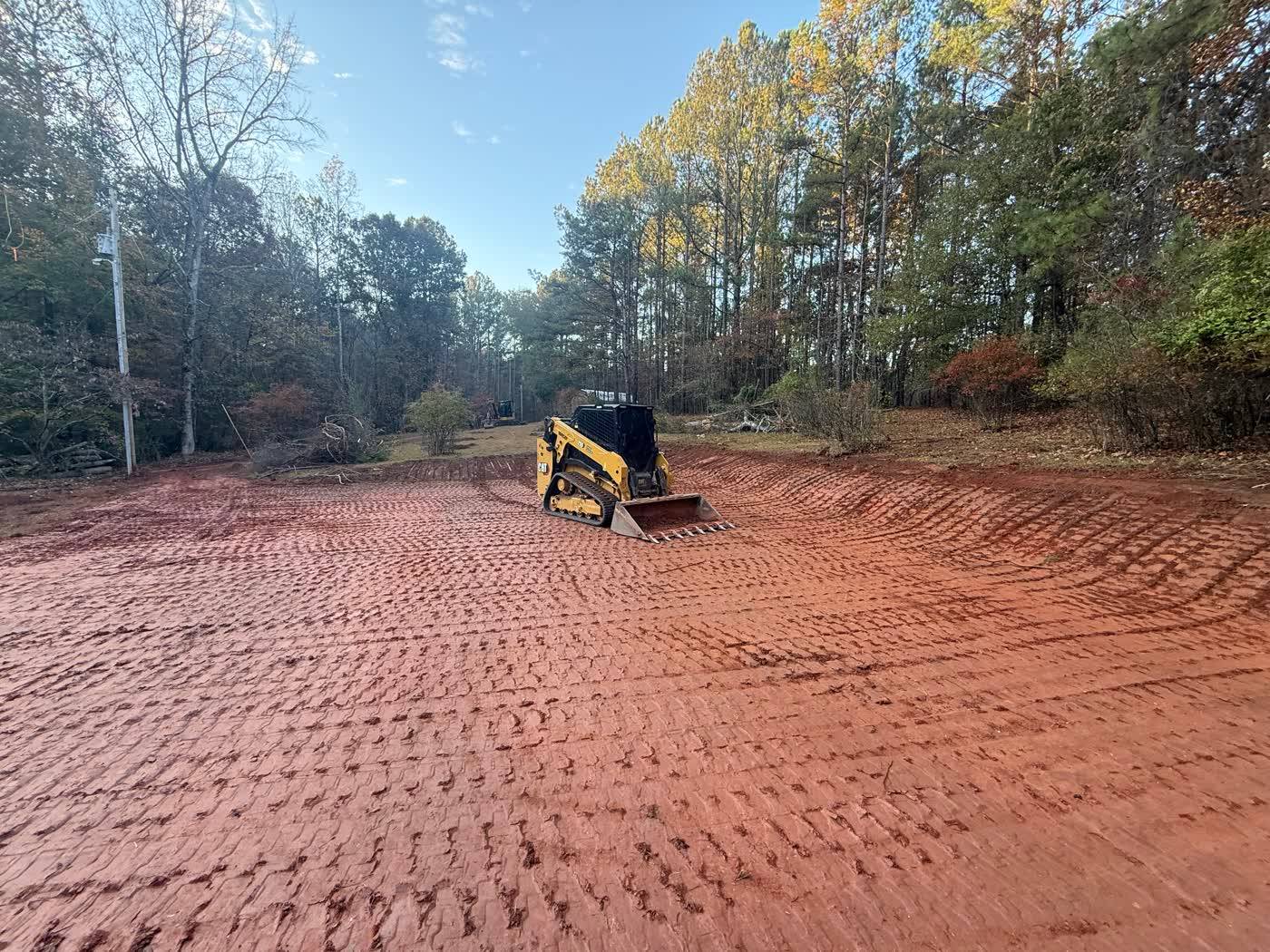 Wide red clay pad graded and tracked out by a skid steer