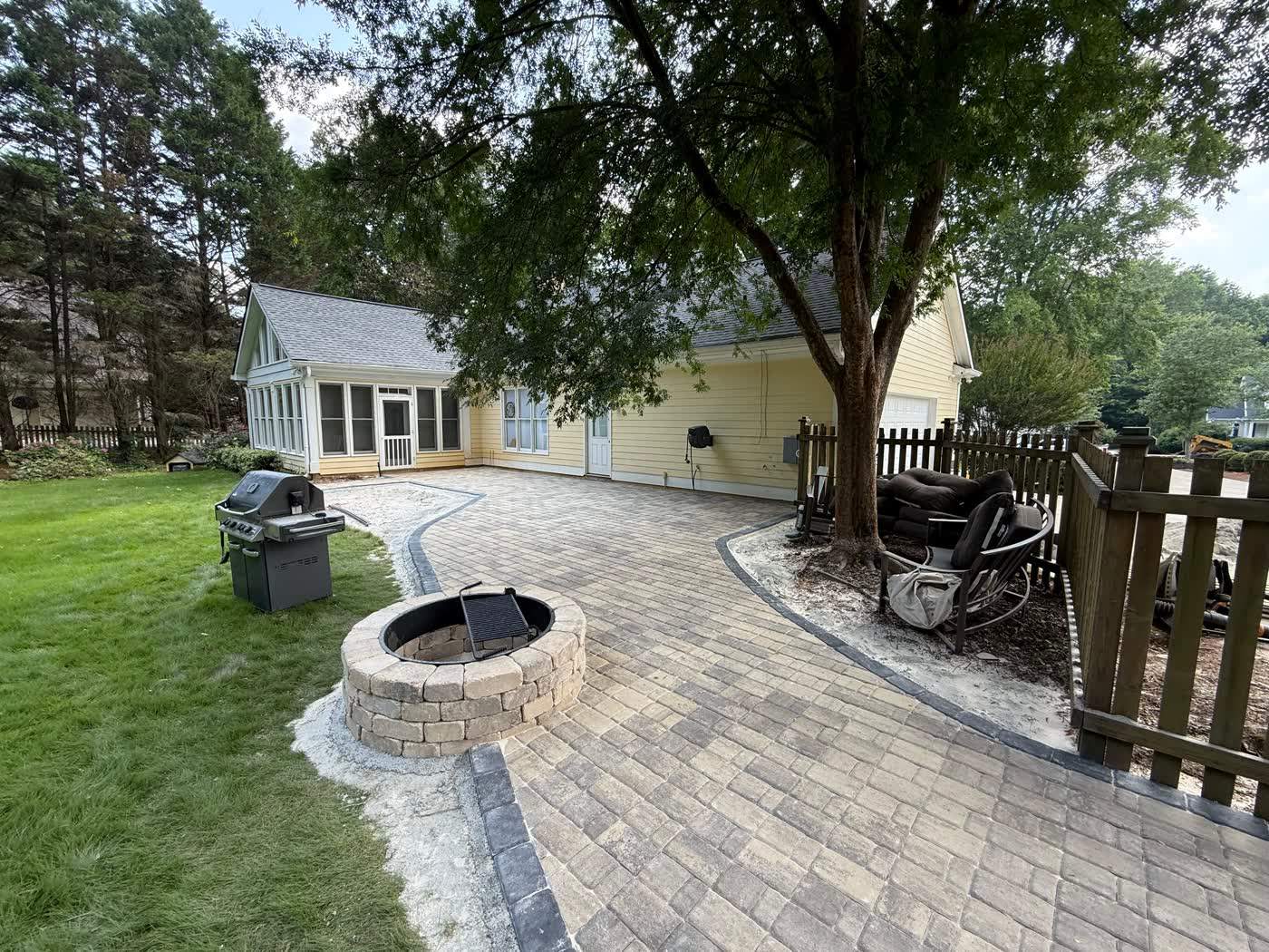 Paver patio with a stacked stone fire pit beside a fenced yard
