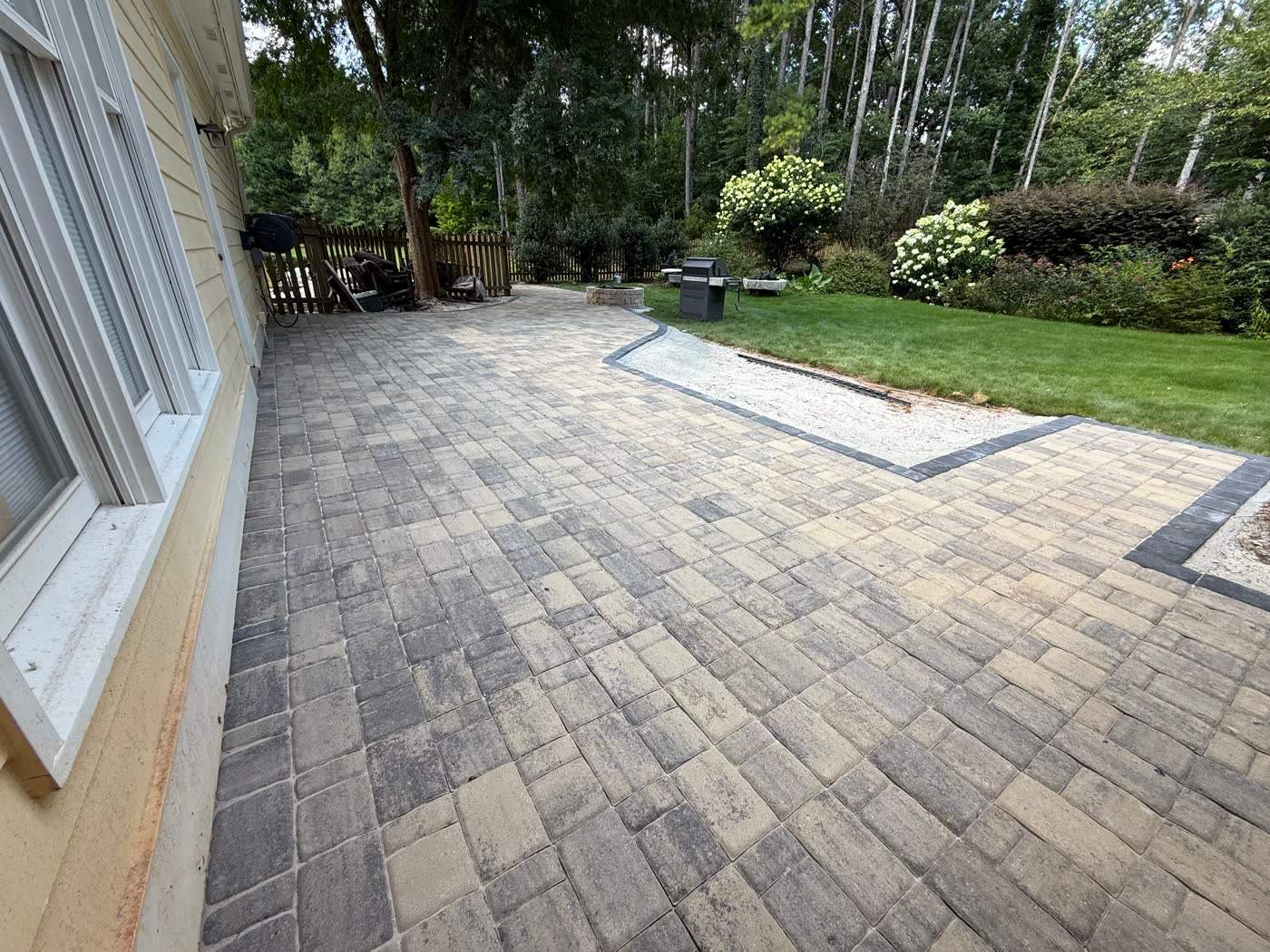 Wide paver patio laid along the back of a house
