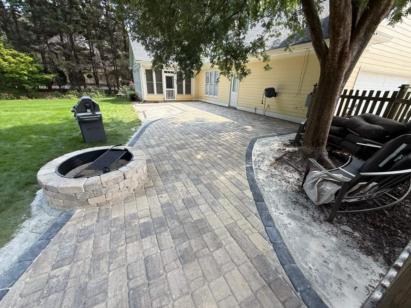Paver patio and fire pit set into a back lawn
