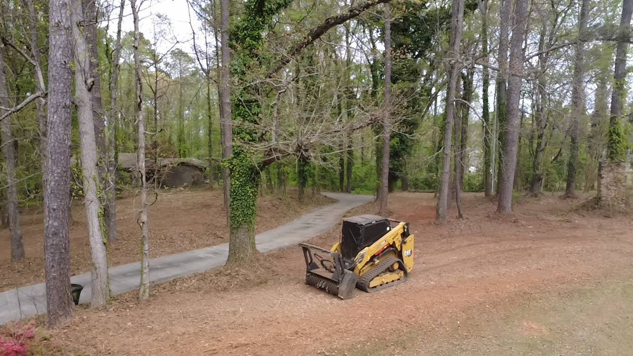 Tracked skid steer running a forestry mulching head through a wooded lot