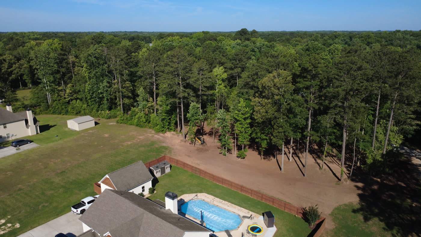 Aerial view of a backyard pool with the treeline cleared and mulched behind it