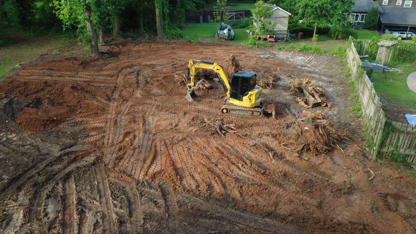 Aerial view of an excavator clearing stumps on a red clay lot