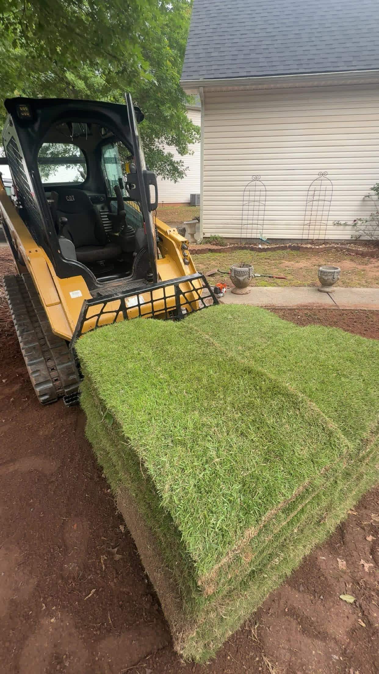 Skid steer carrying a pallet of sod across a job site