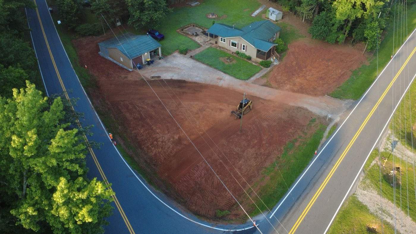 Wide red clay pad graded and tracked out by a skid steer